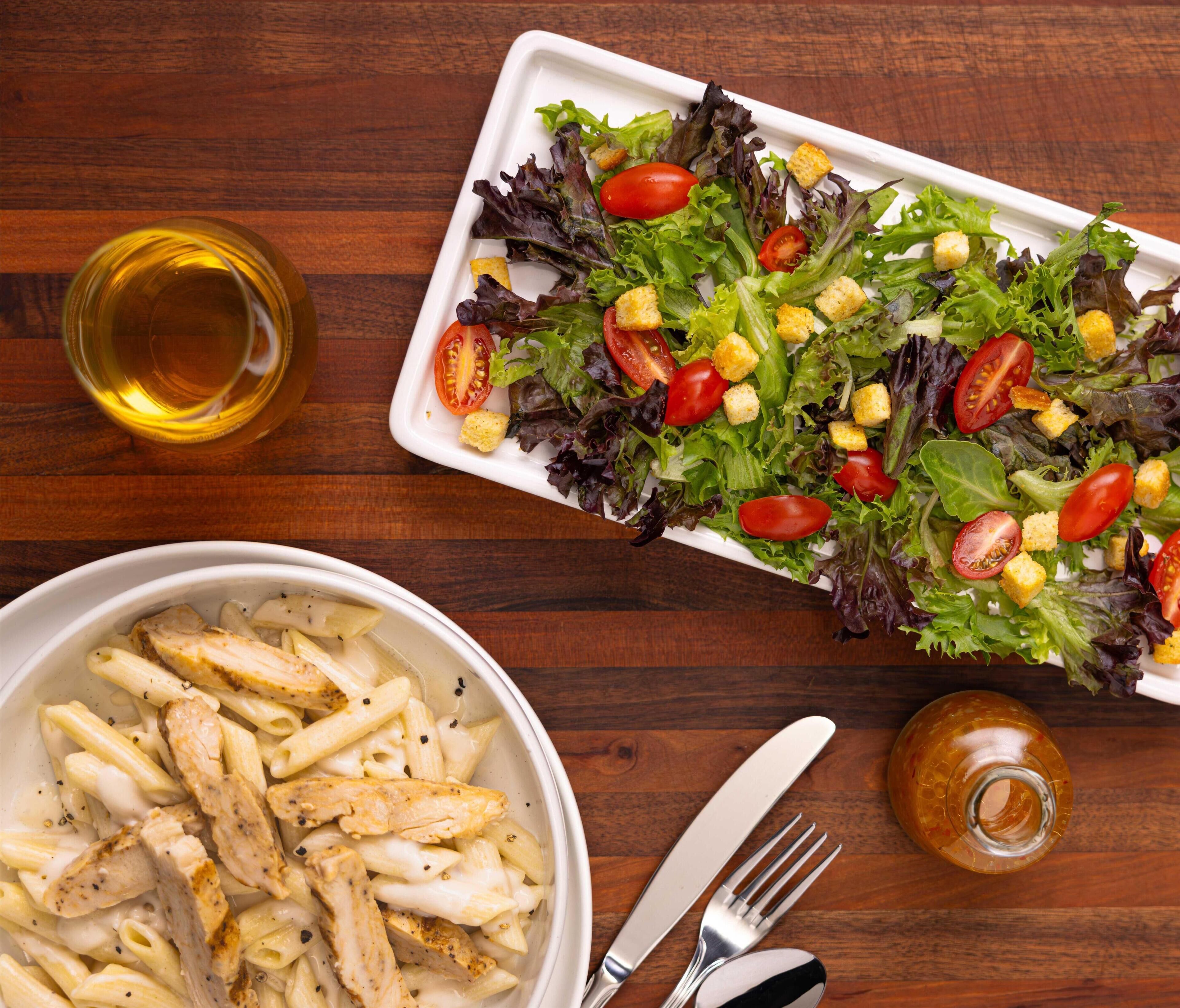 A meal with pasta, salad, and a drink on a wooden table.