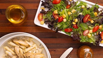 Un pasto con pasta, insalata e una bevanda su un tavolo di legno.