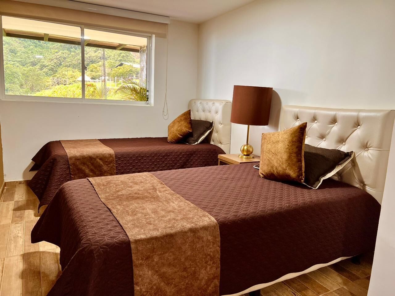 A hotel room with two beds, a window with a view, a lamp, and a nightstand.
