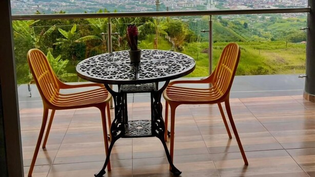 A balcony with a round table and two chairs, overlooking a cityscape and greenery. - SKYGREEN ECOHOTEL (Dosquebradas)