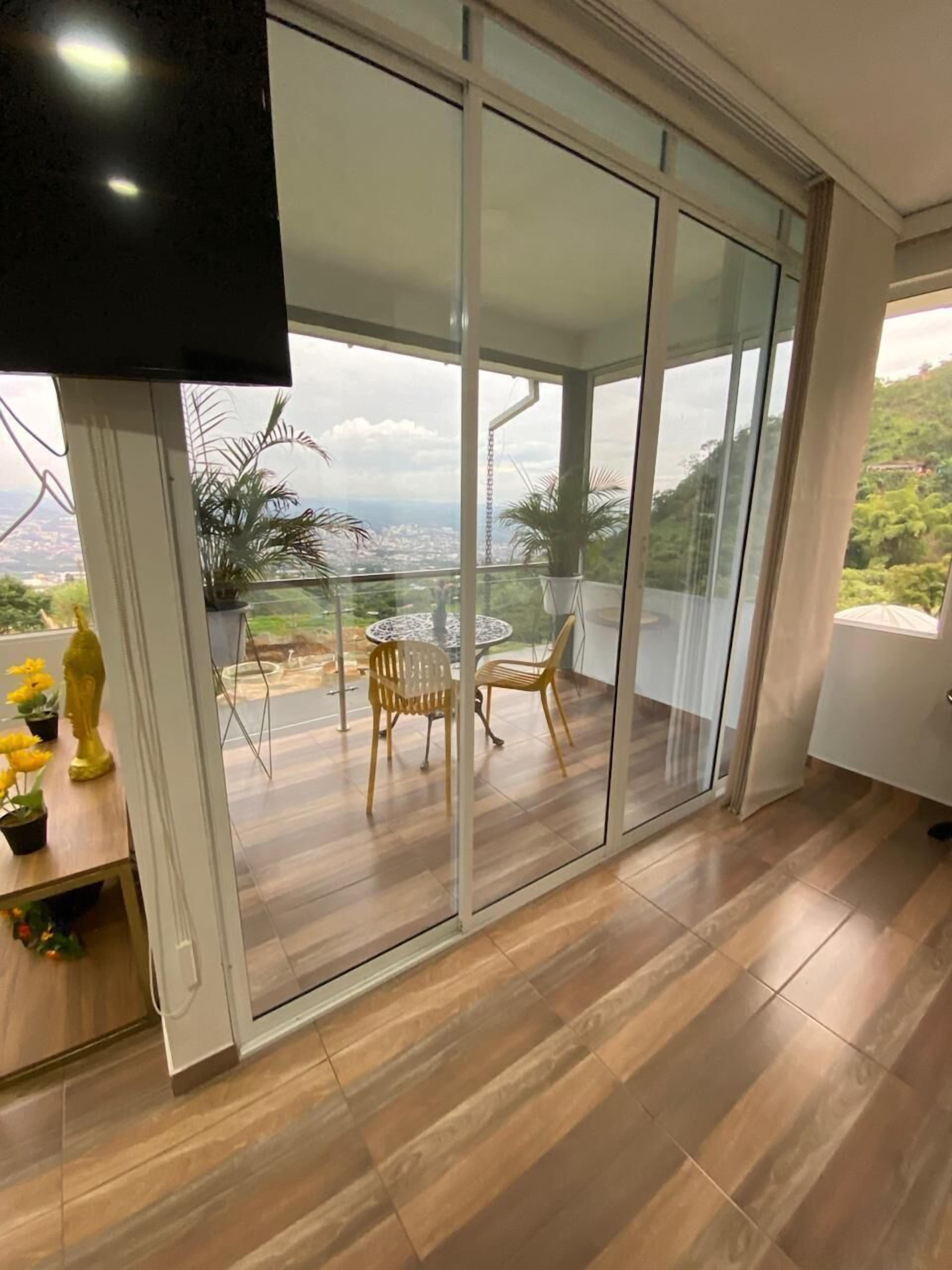 A spacious balcony with a glass door, wooden flooring, and a view of a cityscape.