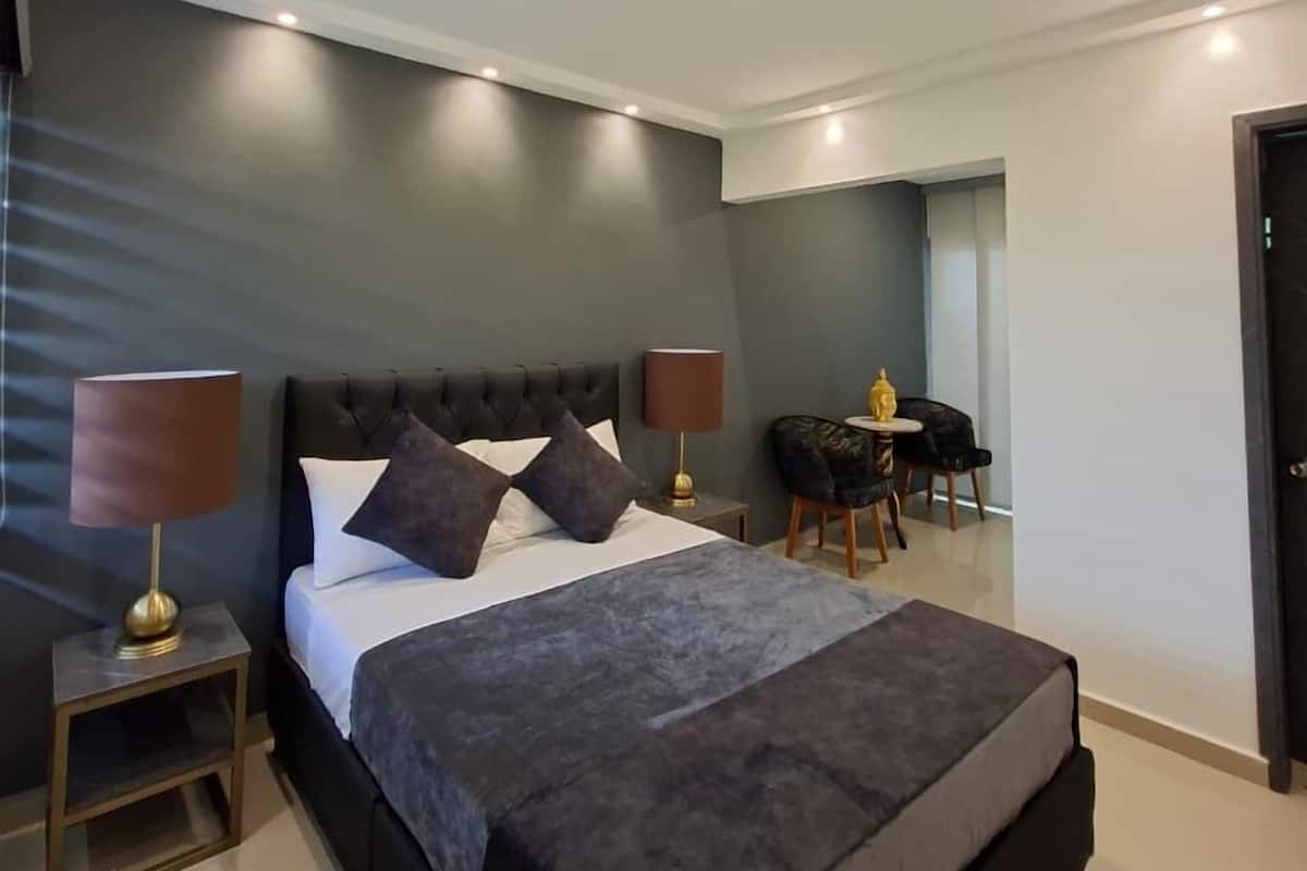 Una habitación de hotel moderna con una cama grande, lámparas de noche, una mesita y una silla.