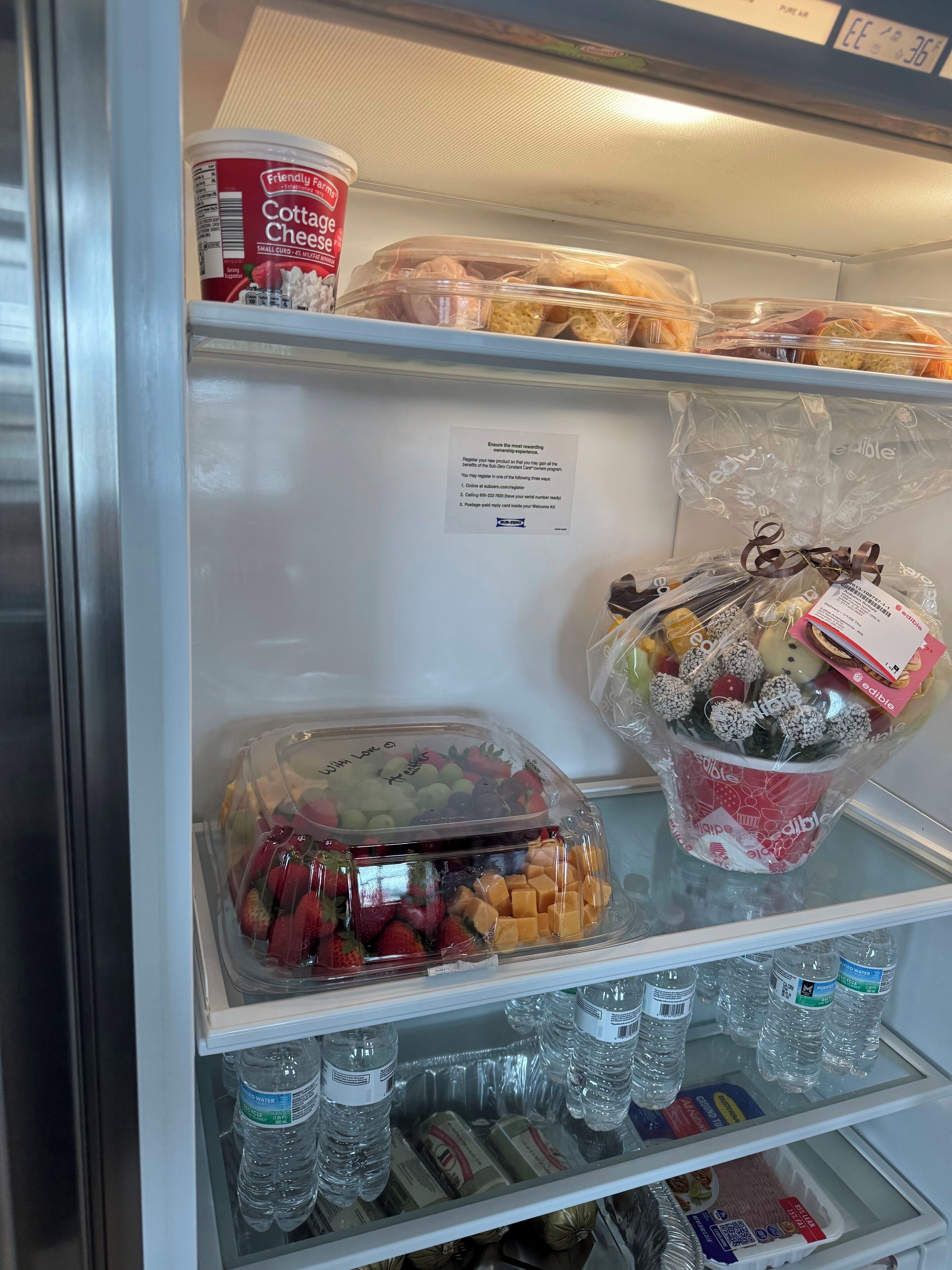 A refrigerated display case with various food items including cottage cheese, bread, fruits, and bottled water.