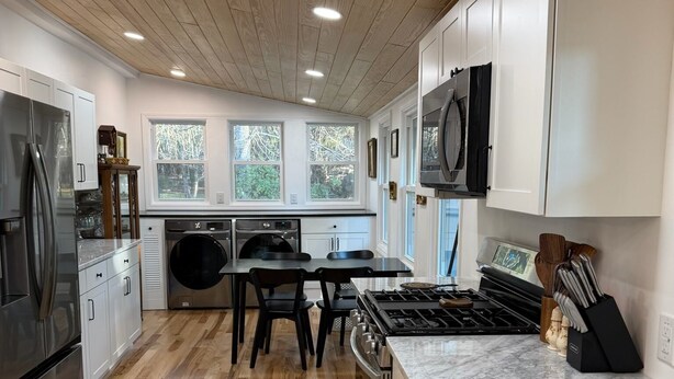 Una cocina moderna con suelo de madera, armarios blancos, electrodomésticos de acero inoxidable y un amplio ventanal que proporciona luz natural.