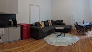 Un espacio habitable compacto con kitchenette, un sofá, una pequeña mesa redonda y un comedor.