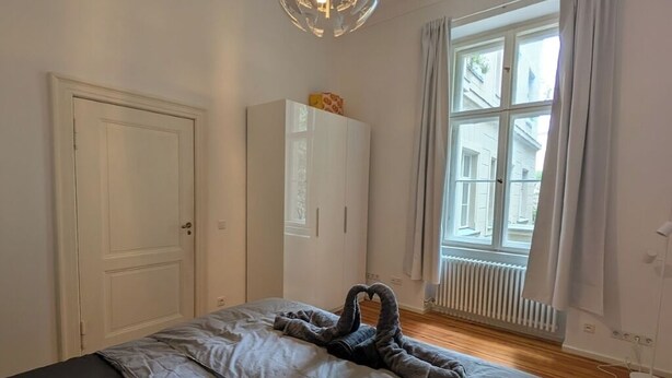 Un dormitorio con cama, armario, radiador y ventana con cortinas.
