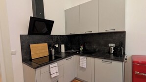 Cocina compacta con gabinetes grises, encimera negra, microondas, tostadora y refrigerador rojo.