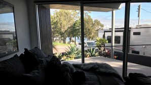 A modern bedroom with a large window, a sofa, and a view of a residential area. - Charming garden suite (Belmont)