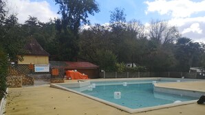Una piscina con un muro de piedra y una zona cubierta con mesas y sillas.