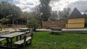 Un espacio al aire libre con césped, mesas de picnic y un pequeño edificio amarillo.