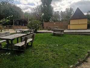 Ein grüner Außenbereich mit Picknicktischen und einem kleinen gelben Gebäude.