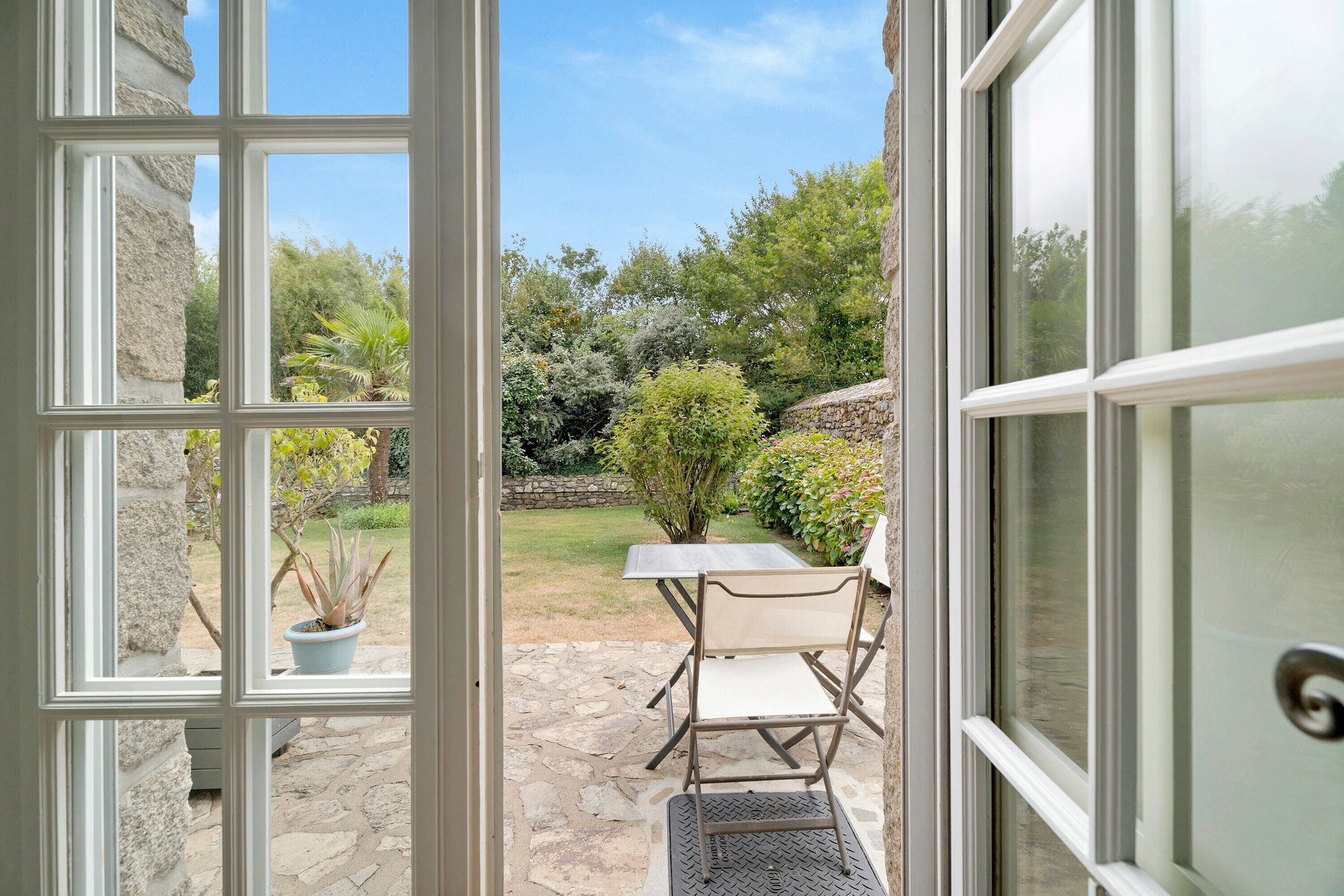 An open door to a patio with a stone floor, a table, and a chair.