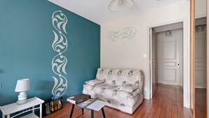Een kamer met een turquoise muur, een witte bank met bloemmotieven, een witte tafel met een lamp en een houten vloer.