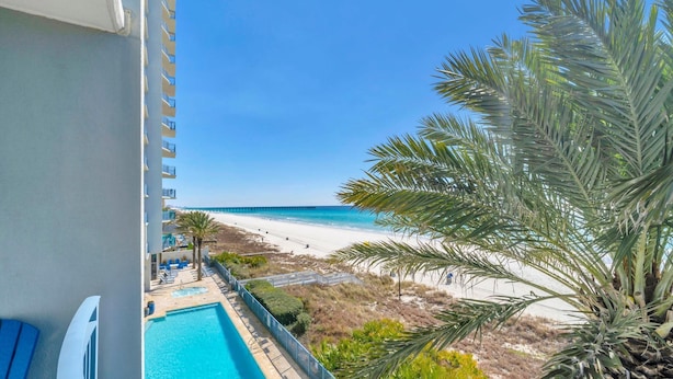 Un balcon avec vue sur une plage, une piscine et un palmier.