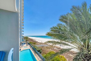 Un balcon avec vue sur une plage, une piscine et un palmier.