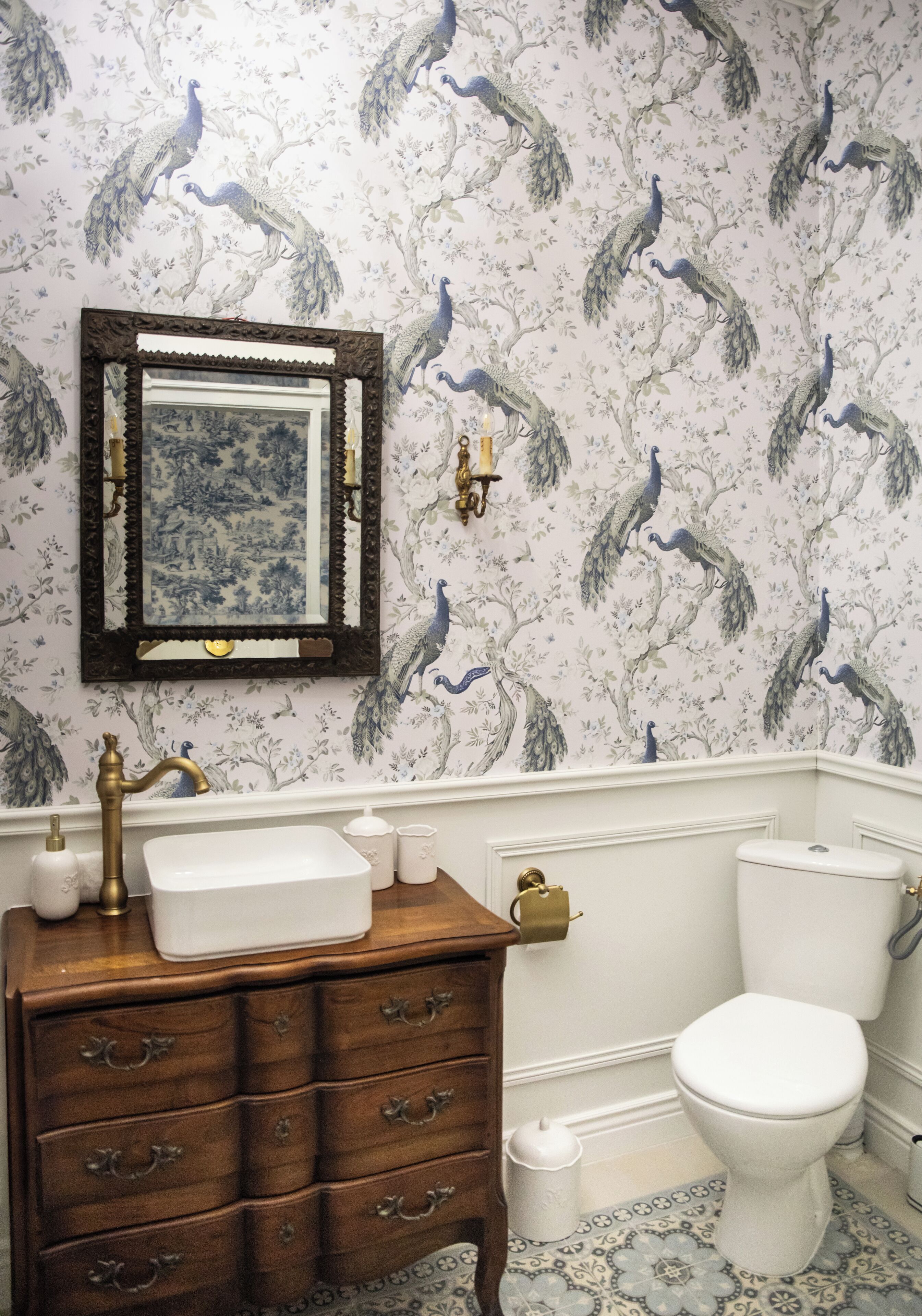 A bathroom with a peacock wallpaper, a wooden vanity with a mirror, a white sink, and a toilet.