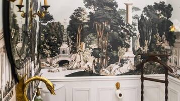 Een badkamer met een rond wastafel, een spiegel met een zwart-wit patroon, en een muurschildering van een parklandschap op de muur.