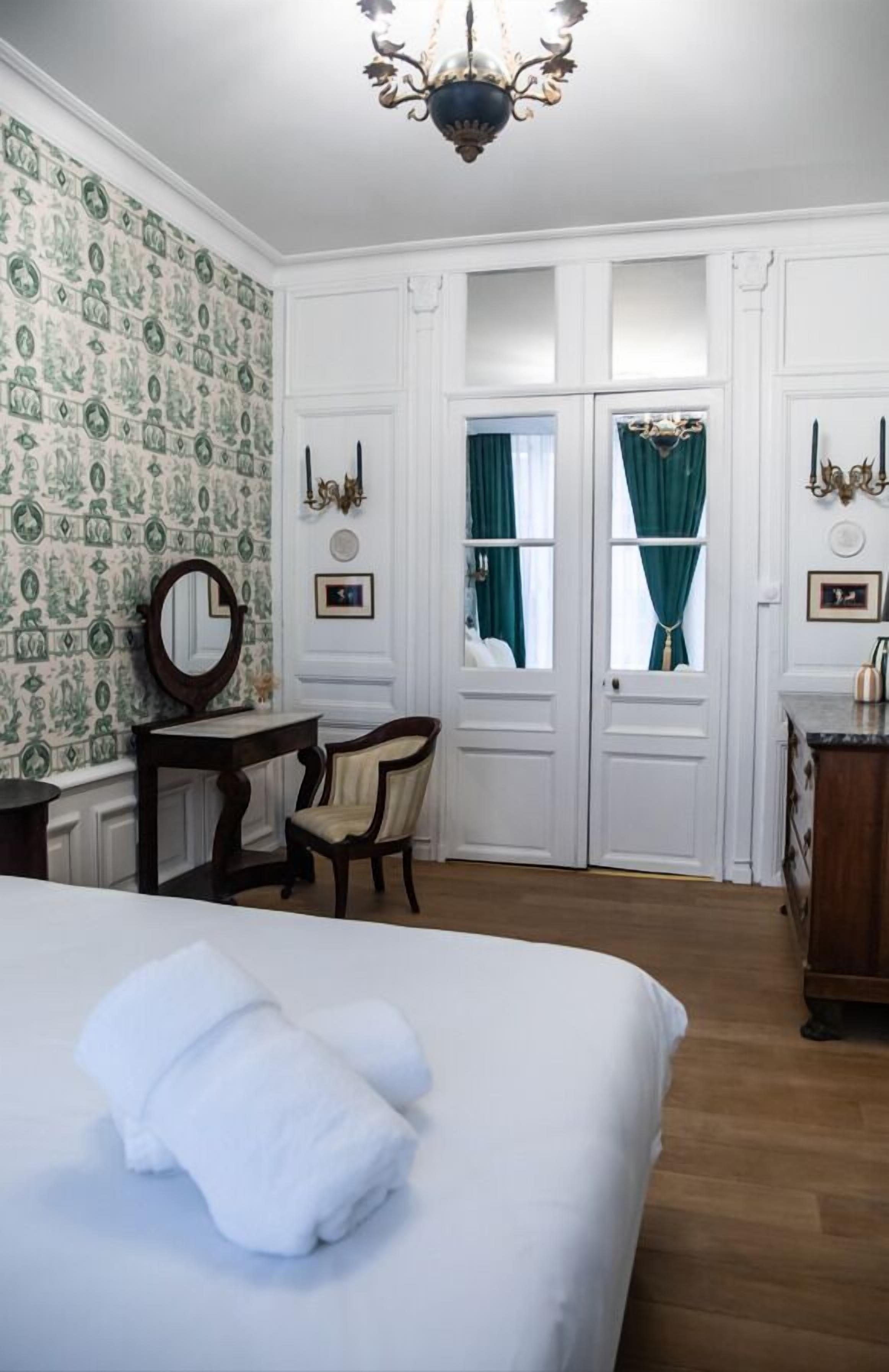 A hotel room with a bed, a desk, a chair, a dresser, and a window with curtains.
