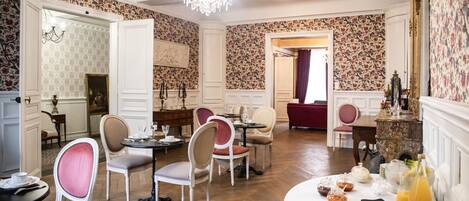 A dining area with a chandelier, floral wallpaper, and a variety of seating arrangements.
