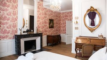 A bedroom with a fireplace, a bed, a desk, and a mirror.
