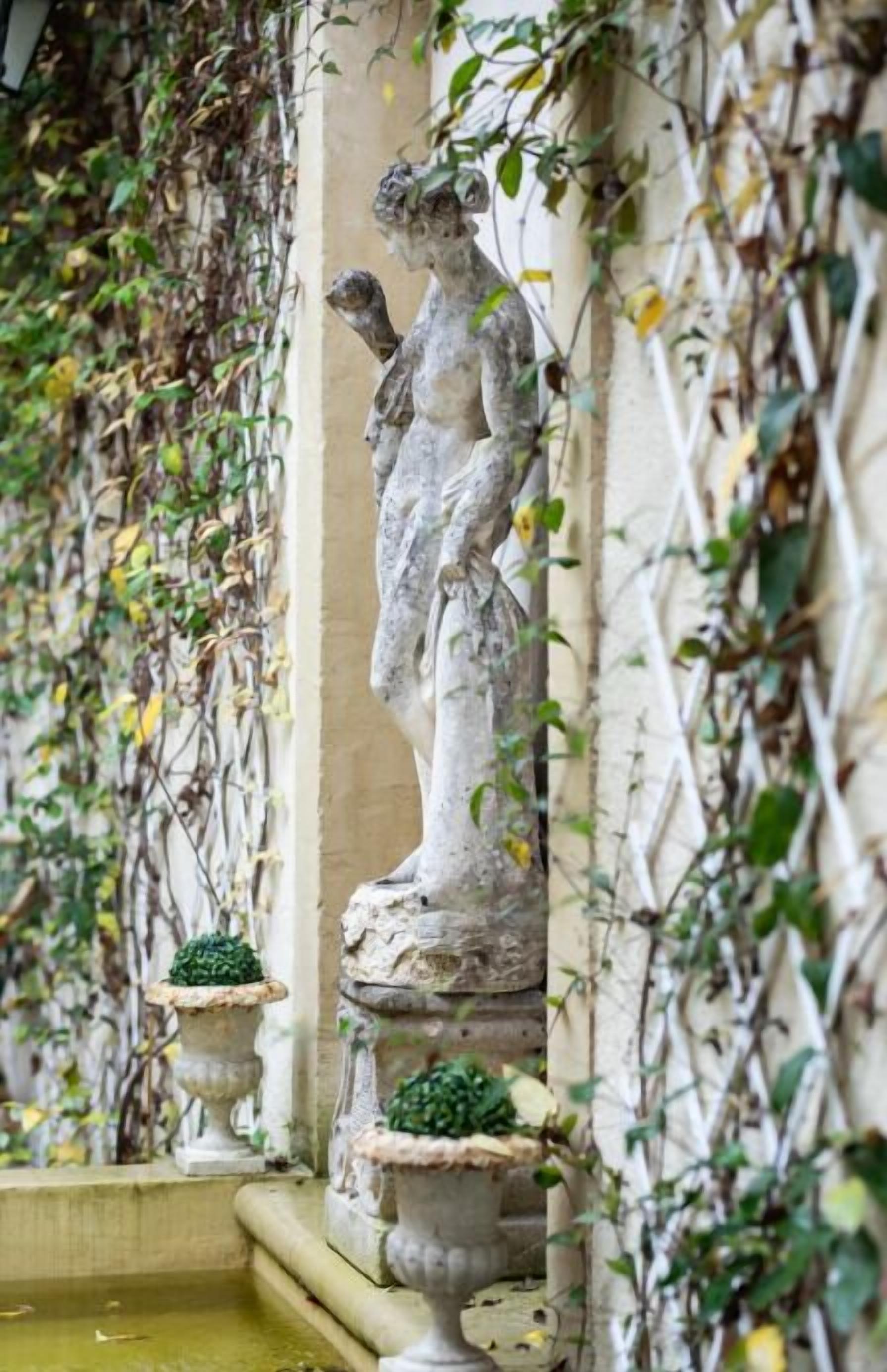 Una fuente de piedra con estatuas y macetas, rodeada de plantas trepadoras.