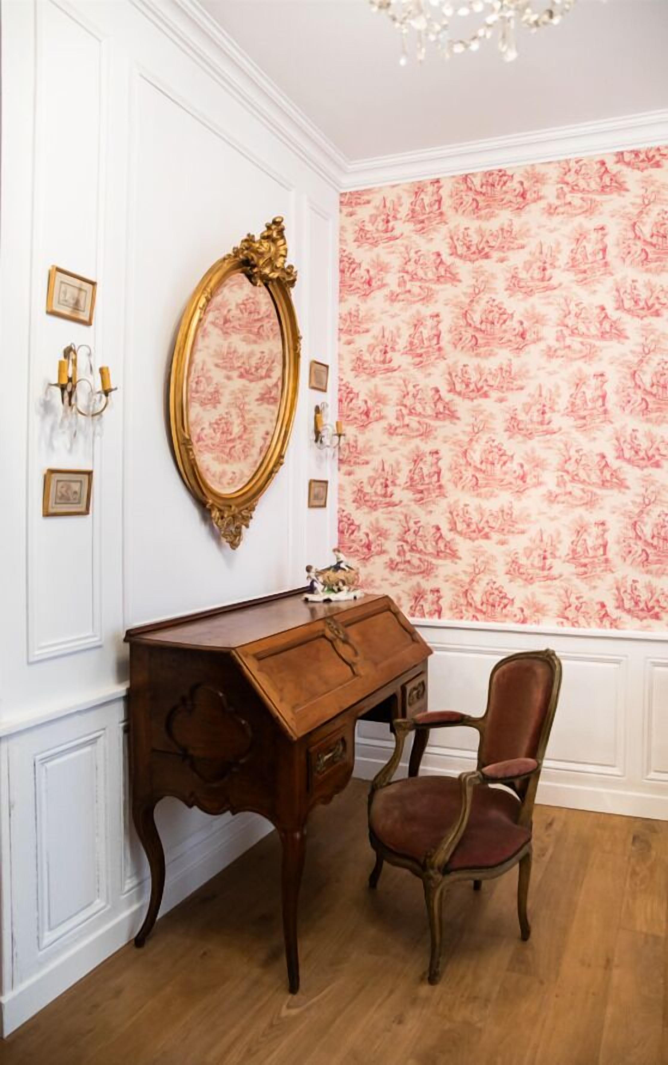 Ein Zimmer mit einem hölzernen Schreibtisch, einem Stuhl, einem großen, verzierten Spiegel und einer Wand mit Muster