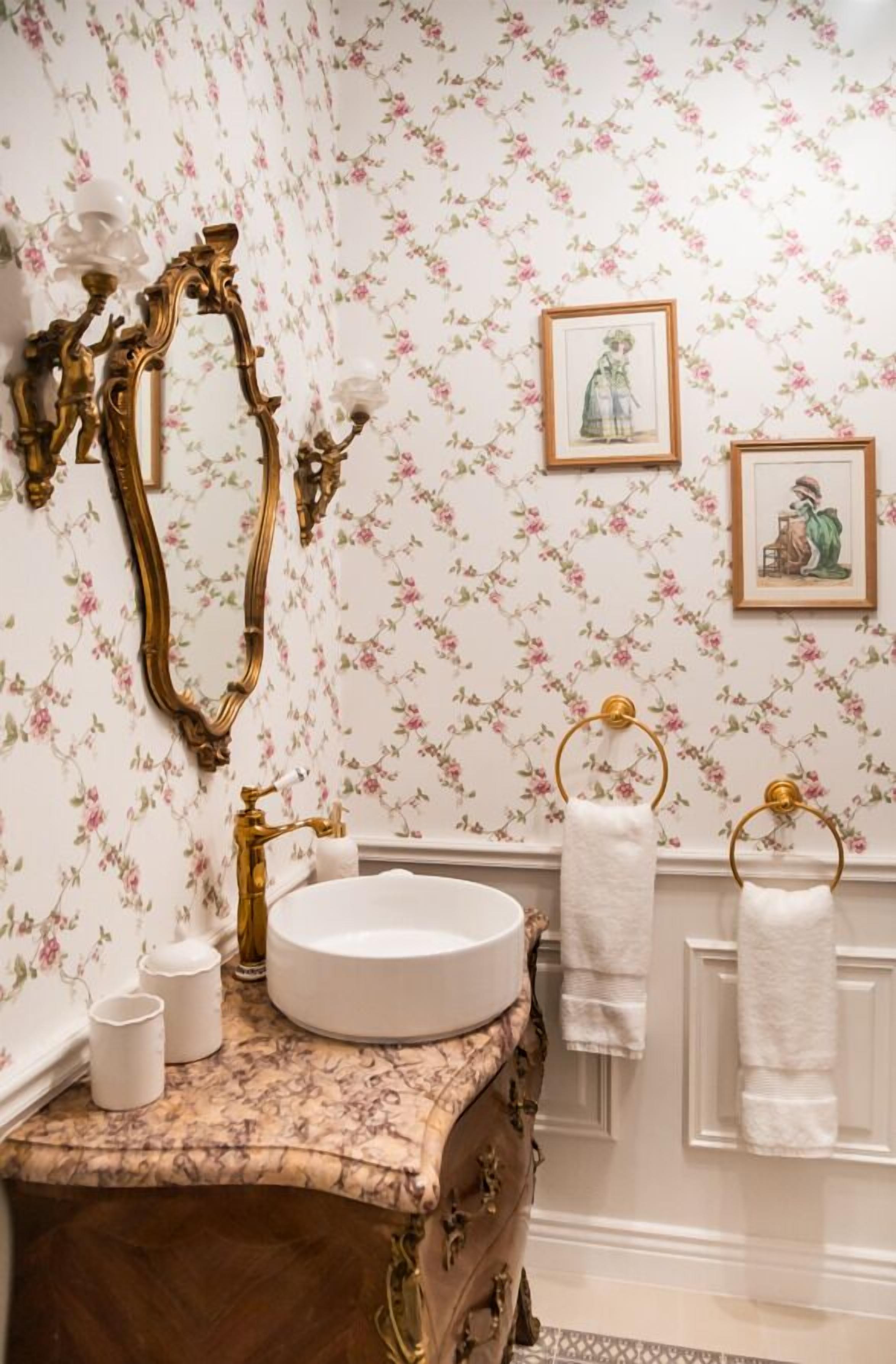 A bathroom with a vintage vanity, floral wallpaper, and framed artwork on the wall.
