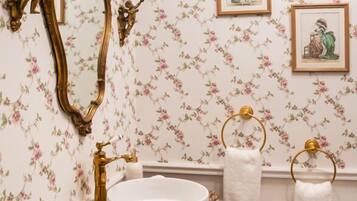 A bathroom with a vintage vanity, floral wallpaper, and framed artwork on the wall.