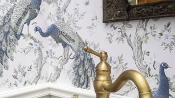 Un baño con un revestimiento decorativo de diseños de pavo real, un grifo dorado y un dispensador de jabón blanco.