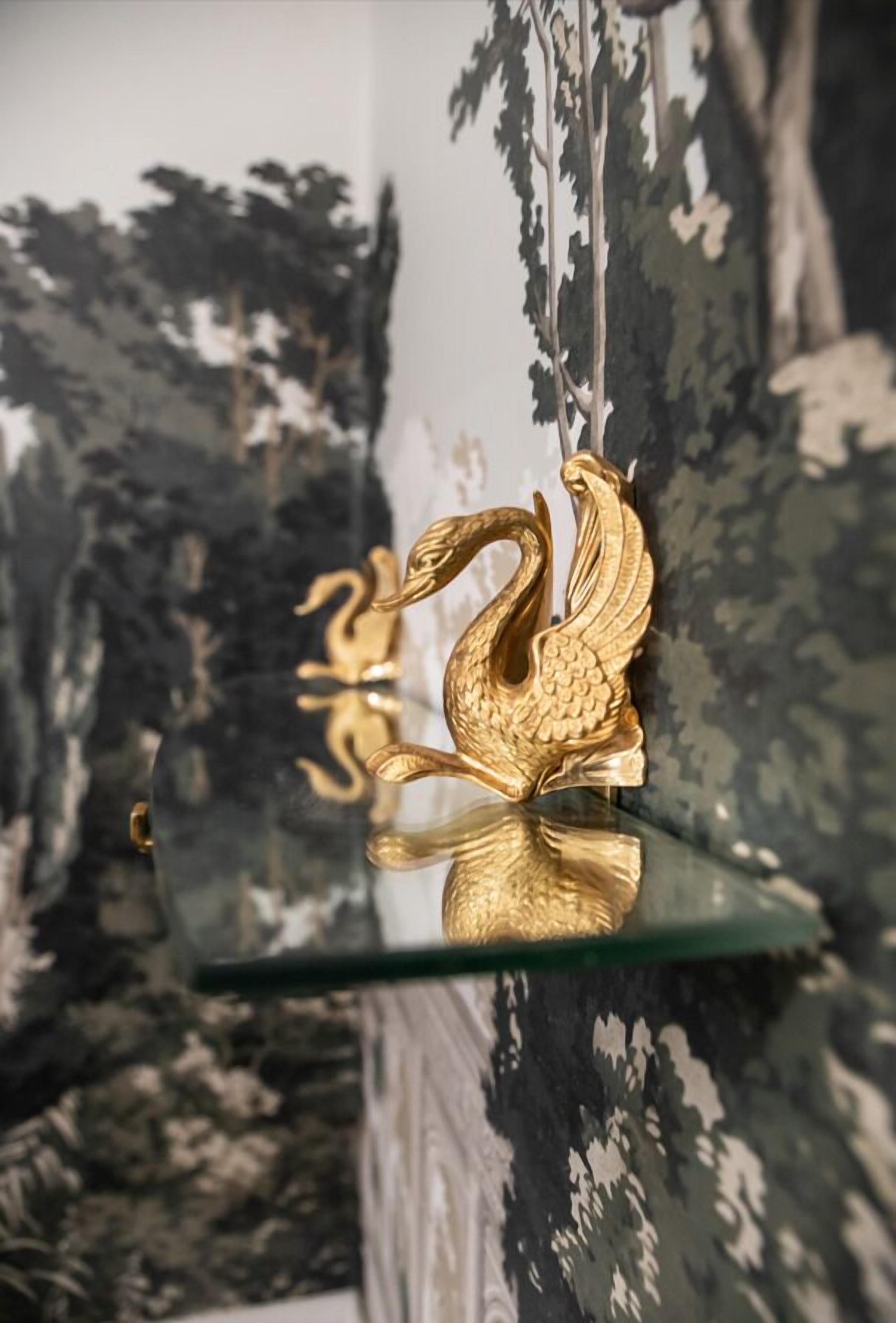 A gold swan-shaped object on a glass shelf against a patterned wall.