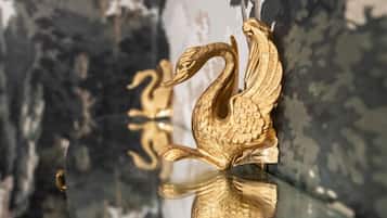 A gold swan-shaped object on a glass shelf against a patterned wall.