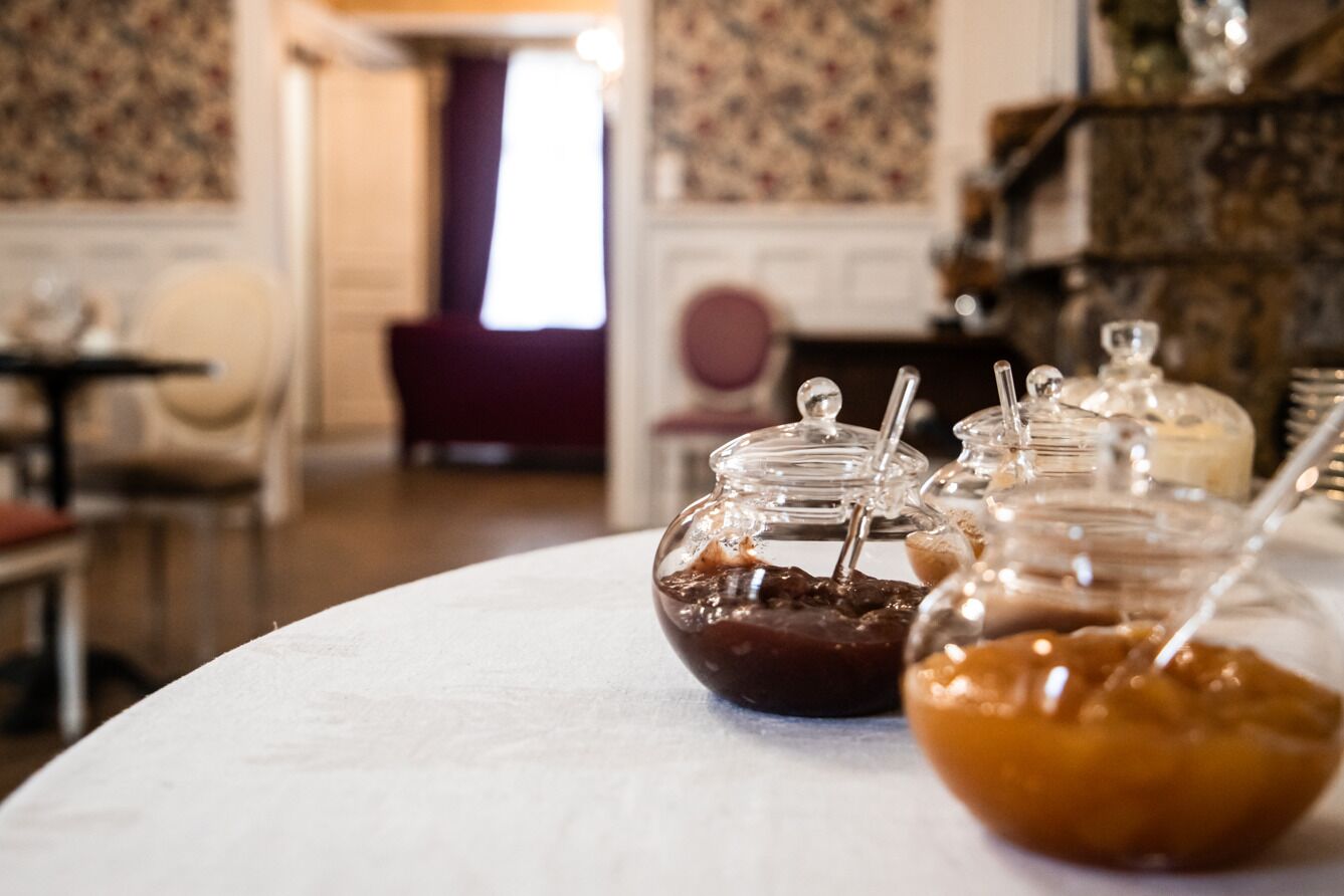 A table with three glass jars containing different sauces, a white tablecloth, and a room with patterned wallpaper and a fireplace.