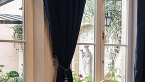 A dining area with a table set for two, a statue visible through the window, and a dog lying on the floor. - Maison La Louise (Ligny-en-Barrois)