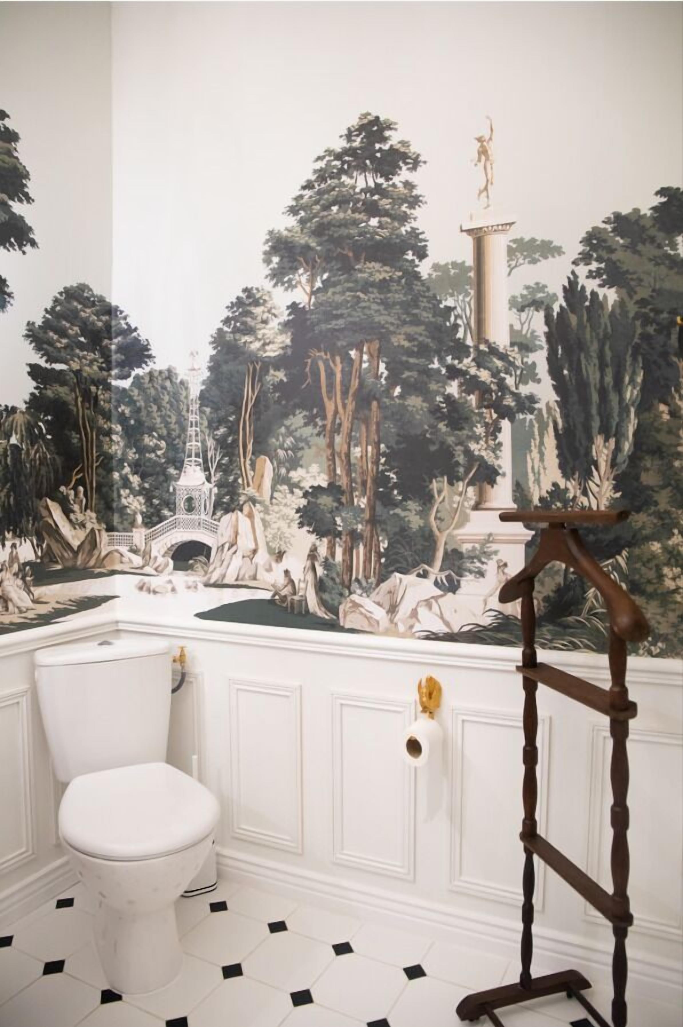 Ein Badezimmer mit einer Wandmalerei von Waldlandschaft, einer weißen Toilette und einem hölzernen Standrohr.