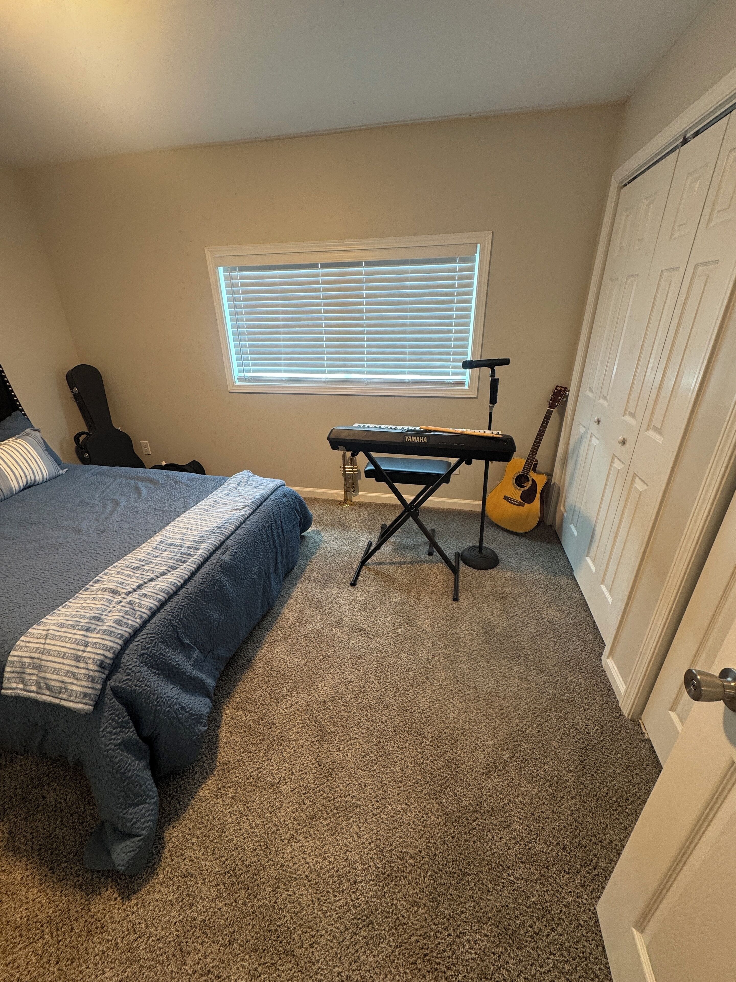 Ein Schlafzimmer mit Bett, Tastatur, Gitarre und einem Fenster mit Jalousien.
