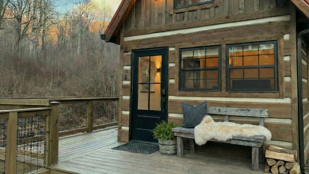 Eine Blockhütte mit einer Holzterrasse, einer Bank, einer Tür und Fenstern.