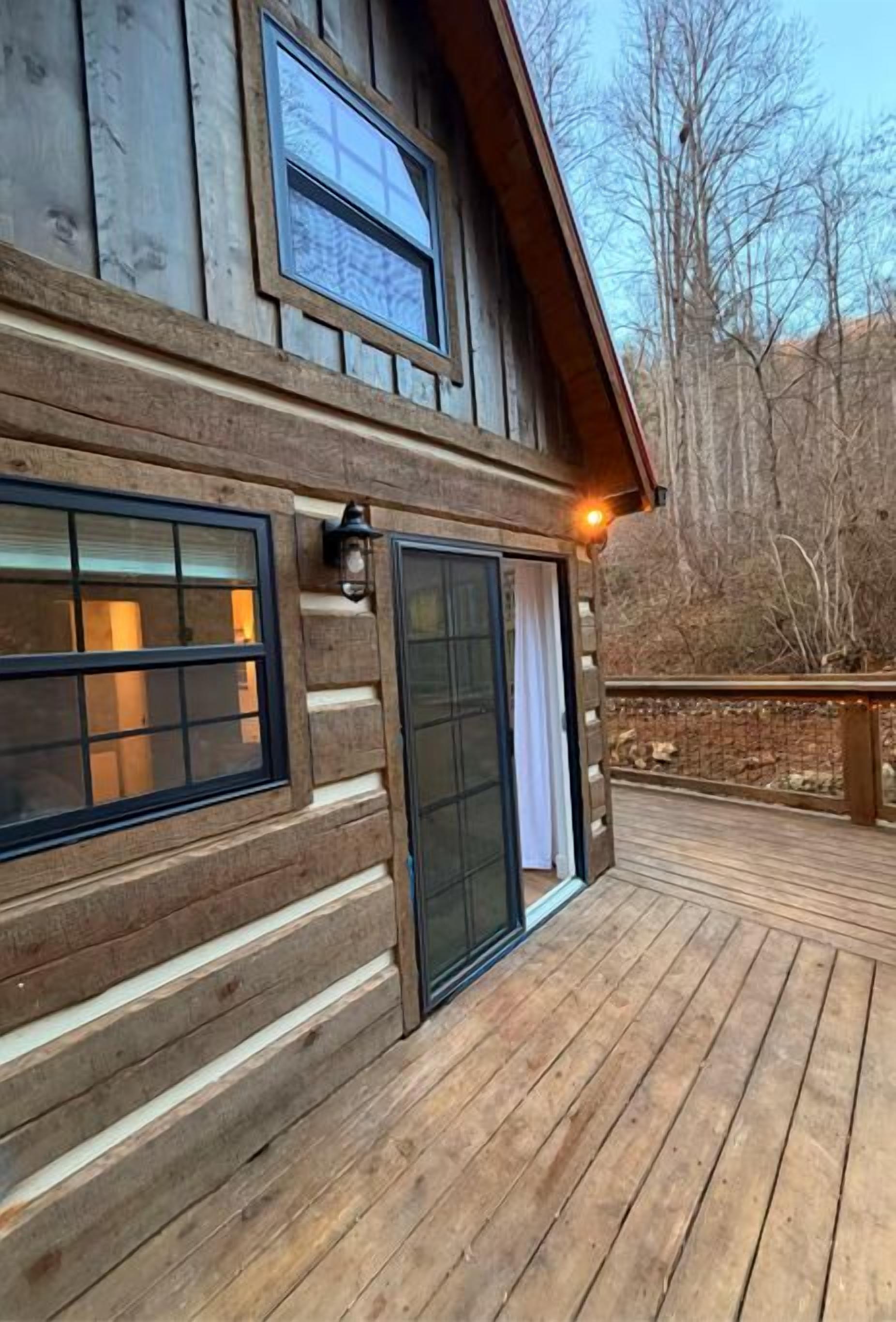 A wooden cabin with a deck, large windows, and a door with a glass panel.