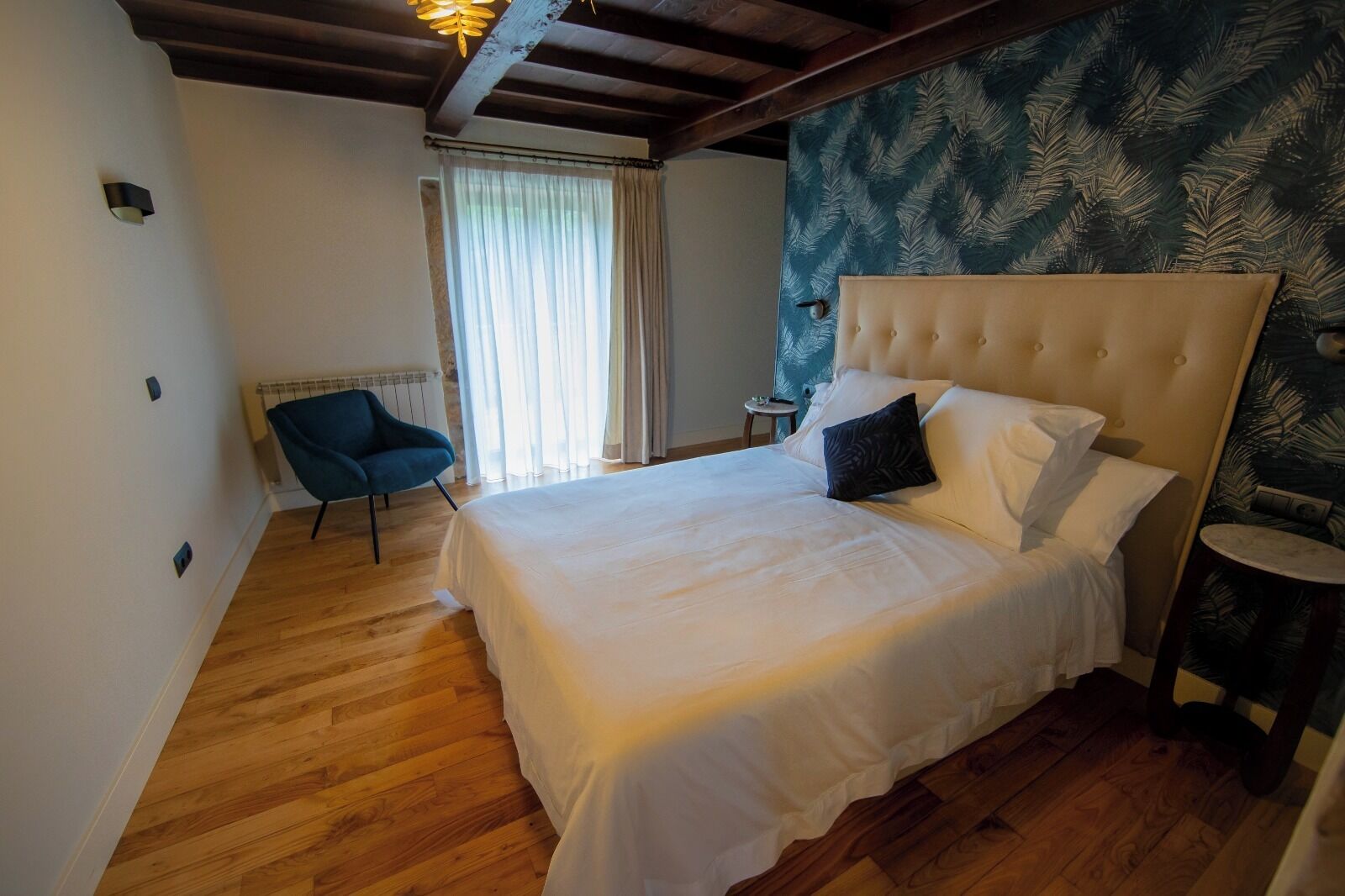 A bedroom with a large bed, a chair, a small table, and a patterned wall.