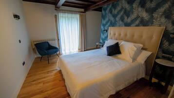 A bedroom with a large bed, a chair, a small table, and a patterned wall.