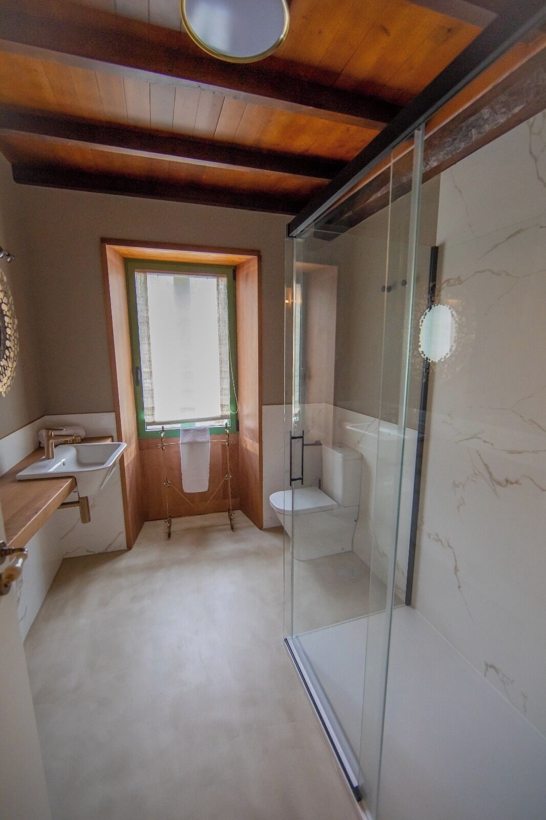 A modern bathroom with a glass shower enclosure, a wooden vanity, and a window providing natural light.