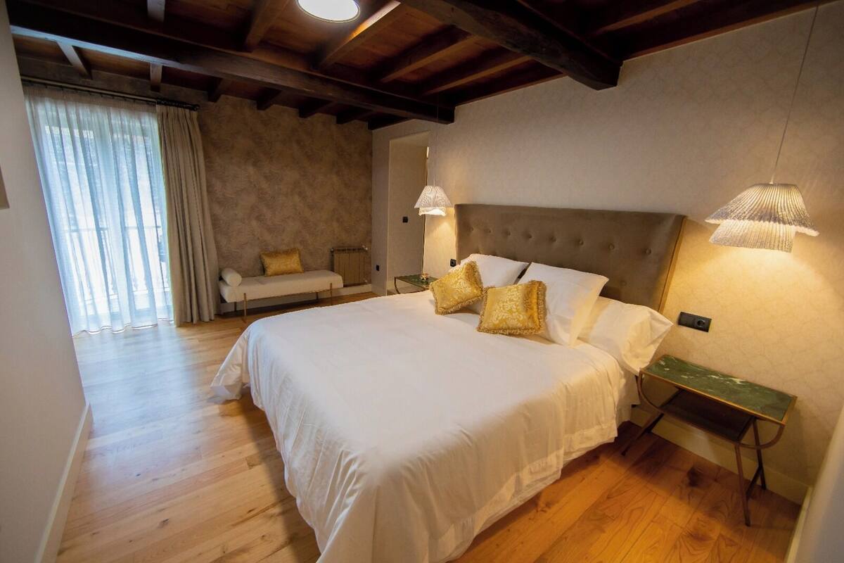 A bedroom with a large bed, a bedside table, a lamp, and a bench.