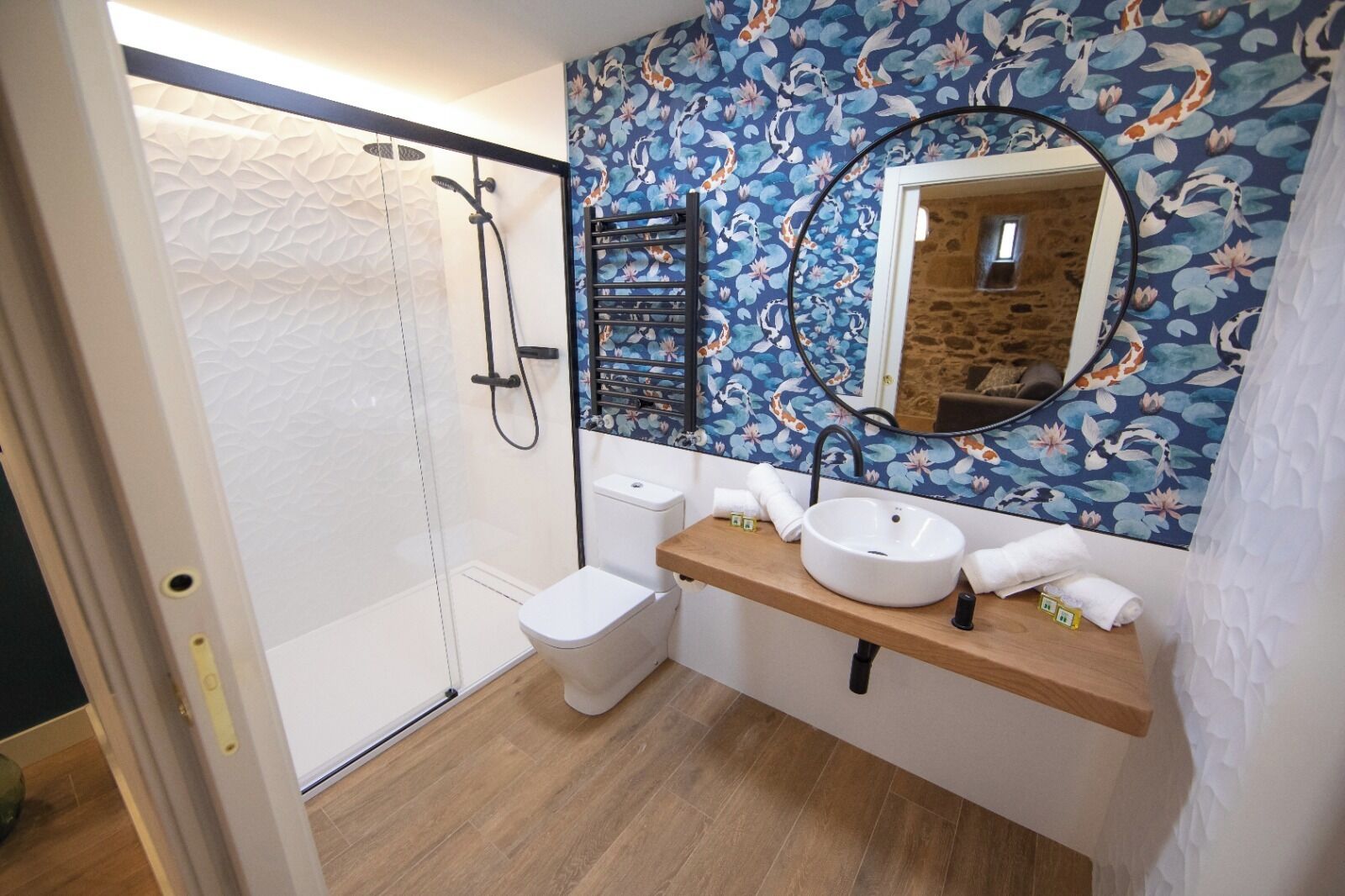 Un baño con ducha envuelta en vidrio, inodoro, lavabo con espejo y tocador de madera.