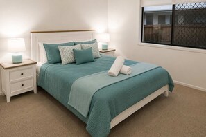 Un lit avec une couvre-lit de couleur turquoise, deux oreillers, une serviette enroulée et deux lampes de chevet.