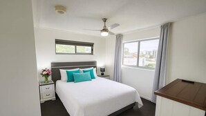 A hotel room with a bed, a nightstand, a desk, a window with curtains, and a ceiling fan. - Central Townsville CBD 1BR Apartment with Pool and Parking (Townsville City)