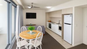 A compact kitchen with a built-in oven, a refrigerator, and a dining area with a table and chairs. - Central Townsville CBD 1BR Apartment with Pool and Parking (Townsville City)
