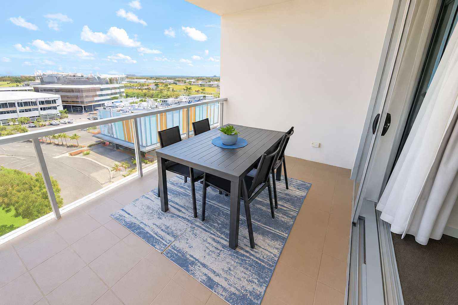A balcony with a table and chairs, a view of buildings, and a clear sky.