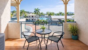 A balcony with two chairs and a table, overlooking a pool and resort area. - Anchorage Escape Townsville | Central Location & Marina Views (South Townsville)