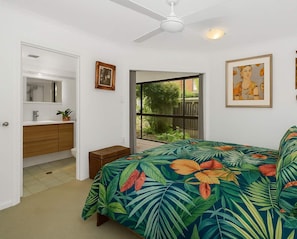 A bedroom with a bed, a window, a ceiling fan, and a bathroom visible through an open door. - North Ward Tropical Escape for 4 – Steps from the Beach & Close to CBD (North Ward)