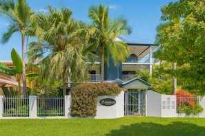 A hotel with a white facade, a gated entrance, and lush greenery including palm trees. - North Ward Tropical Escape for 4 – Steps from the Beach & Close to CBD (North Ward)