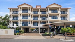 Ein mehrstöckiges Hotel mit zentralem Eingang, Balkonen an jeder Etage und einem überdachten Bereich mit Sitzgelegenheiten.